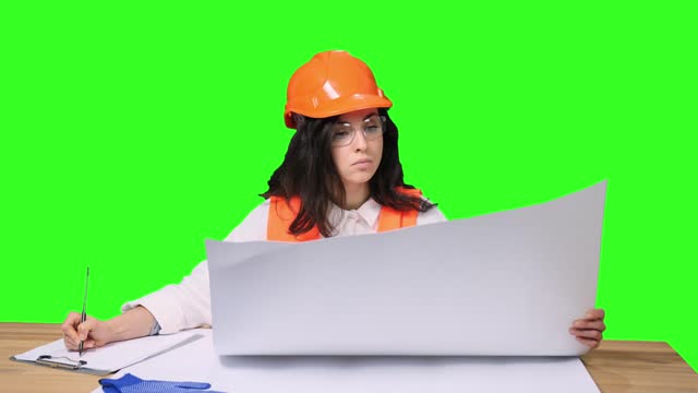 Young female architect with blueprint making notes on the chroma key