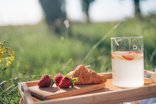 Image a strawberry croissant on a wooden table and a jug with lemonade.