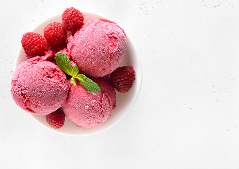 Raspberry ice cream scoop with fresh berries in bowl over white stone background with copy space. Top view, flat lay