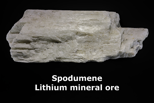 Crystal mineral spodumene, with text. Commercially mined source of lithium (Li). Black background. Copy space.