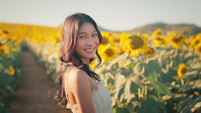 Happy asian woman smiling in sunflower field outdoors, Cheerful Young female looking at the camera feeling free in blooming garden in summer day