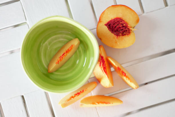 Sliced fresh yellow peach in bright blue ceramic bowl on white kitchen table. Healthy eating, raw food, fruit dieting. High quality photo