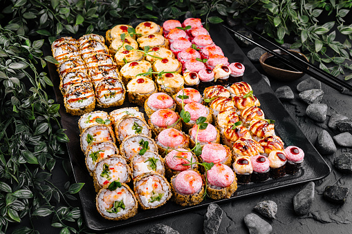 Colorful variety of sushi and rolls beautifully presented on a slate tray amidst green leaves