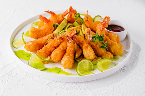 Golden fried shrimp served with slices of fresh lime and dipping sauce, garnished with herbs