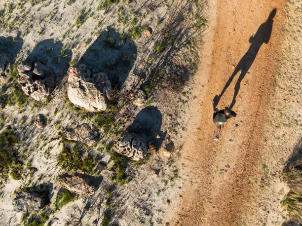 Drone view of runner on dirt road in mountains with hard shadow