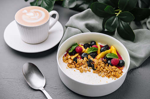 Nourishing bowl of yogurt with granola and berries paired with a latte on a minimalistic grey backdrop