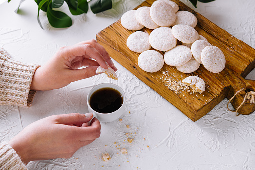 Close-up of hands holding coffee beside powdered sugar cookies on a wooden board