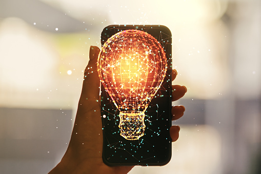 Creative light bulb illustration and hand with mobile phone on background, future technology concept. Multiexposure
