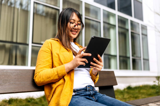 istock Young beautiful woman using digital tablet while sitting on a bench outdoors 2148685904