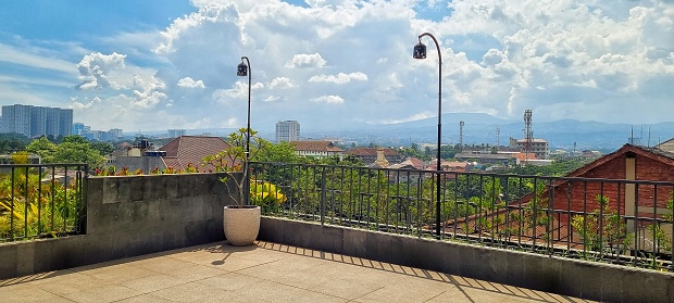 Bandung, Indonesia - Jun 23, 2022: Picture of roof top terrace area during midday with city dense area, blue sky and white clouds as the background