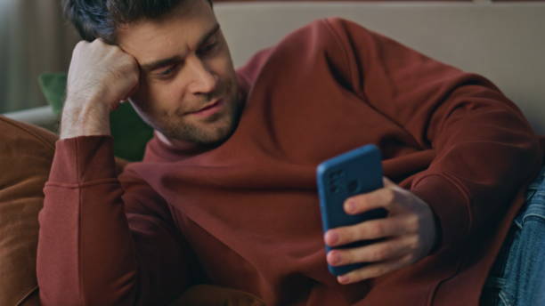 istock Bored man browsing mobile phone app lying couch close up. Guy looking smartphone 2148688652
