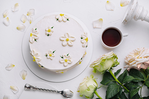 Top view of a beautifully decorated cake with flowers, alongside tea and roses on a white background