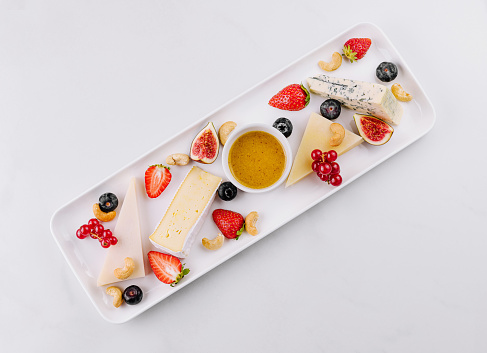 Elegant white platter featuring an assortment of fine cheeses, fresh berries, and a bowl of honey