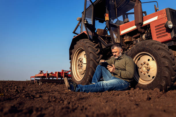 istock Farmer siting and using tablet while resting after cultivation of soil leaning on tractor tire. 2148689151
