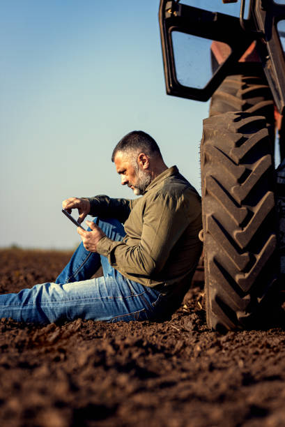 istock Farmer siting and using tablet while resting after cultivation of soil leaning on tractor tire. 2148689152