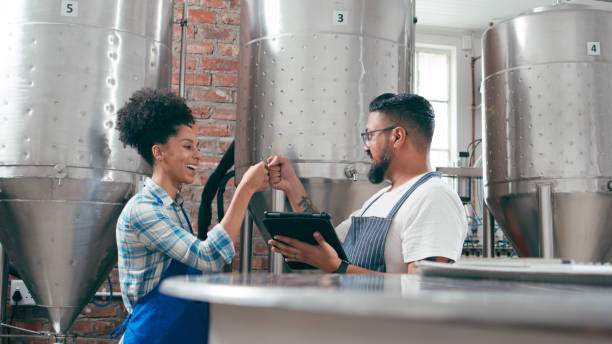 istock Two craft brewers in a local beer brewery, checking production processes on a tablet. Stainless steel fermentation tanks and industrial interior in the background create an authentic brewery scene. 2148689991