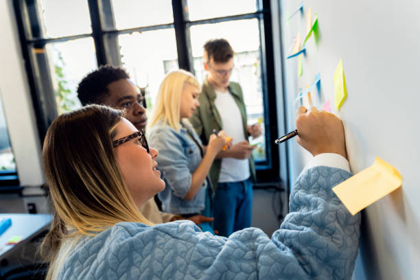 istock Diverse group of young business people working in office using colorful sticky notes on wall to organize their ideas. 2148690213