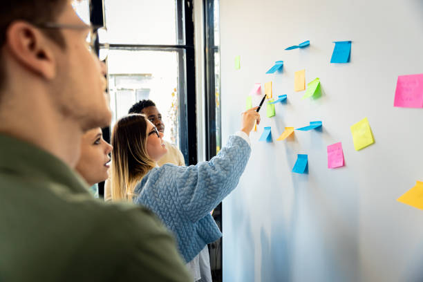 istock Diverse group of young business people working in office using colorful sticky notes on wall to organize their ideas. 2148690217