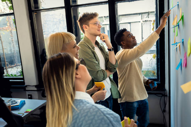 istock Diverse group of young business people working in office using colorful sticky notes on wall to organize their ideas. 2148690223