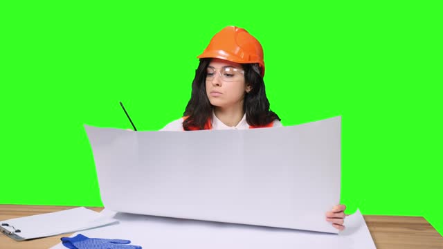 Female construction specialist in hardhat sitting at desk on the chroma key