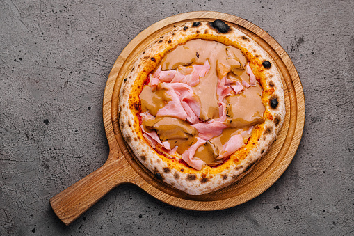 Top view of a delicious ham pizza served on a rustic wooden board, ready to be enjoyed