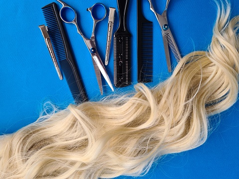A collection of scissors scattered on a vibrant blue surface alongside cut strands of hair