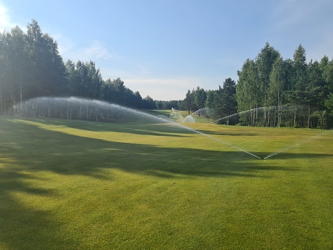 A sprinkler system is actively spraying water onto a well-manicured golf course
