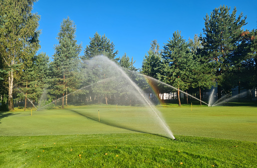 A sprinkler system is actively spraying water onto a lush green golf course