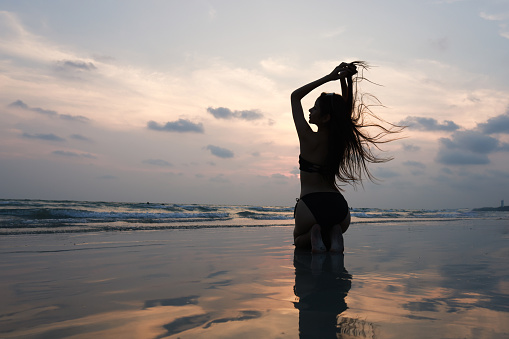 Silhouette of a beautiful woman   sitting on the beach posing to take a photo at sunset on her vacation