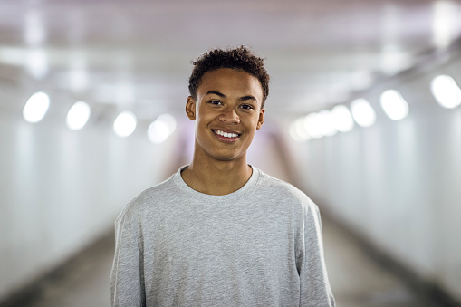 A selective focus front view portrait of a young teenage boy looking at the camera and smiling. He is wearing causal clothing and is stood in an underpass in Newcastle upon Tyne