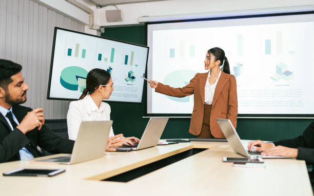 istock A cheerful and confident Asian businesswoman stands, present bar charts data from projector screen to her office colleagues. Asian business women leader role at the meeting. 2148696082