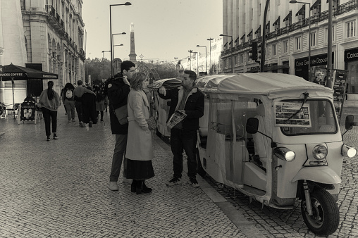 Lisbon, Portugal - December 23, 2023: A tuk-tuk driver talks with clients in a street in Lisbon downtown.
