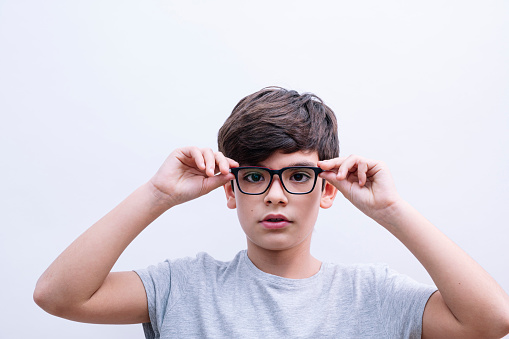 Beautiful child boy student putting on glasses and with backpack on isolated white background