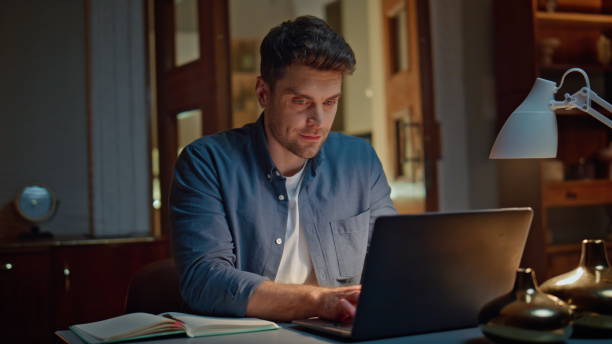 istock Smiling businessman browsing computer texting email at cozy dark flat closeup 2148699446