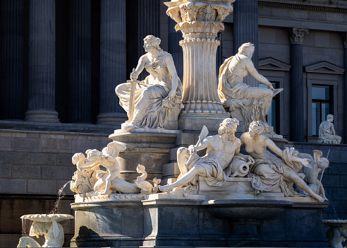 19th century Pallas Athena fountain statues by Carl Kundmann showing allegory of democratic virtues in front of the Austrian Parliament building from 1883 in contrasty sunset light