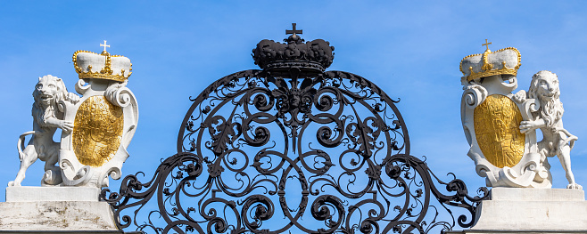 Two lion statues standing on hind legs and holding gilded coats of arms on historical 18th century street gate with ornate baroque iron grill. Outside gate of Belvedere public gardens in Vienna, Austria