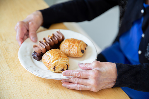 Close of of a variety of sweet desserts a chocolate cake and two chocolate croissants on a plate with a woman's elderly hands surrounding it