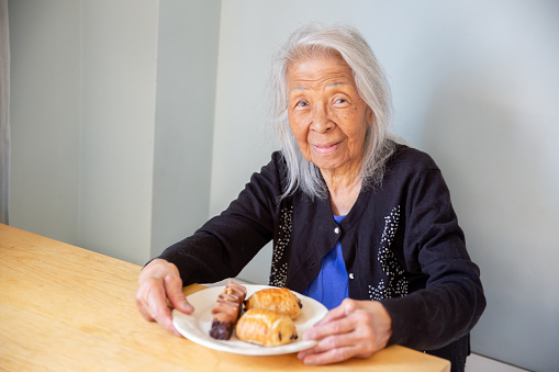 Elderly Filipino woman sits with a plate of dessert and pastries, a chocolate cake and chocolate croissant