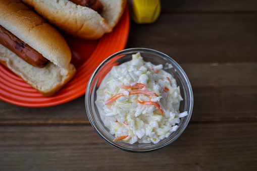 A bowl of coleslaw with hotdogs on a table