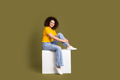Full length body photo of attractive young woman sitting podium cube candid person model posing isolated on khaki color background.