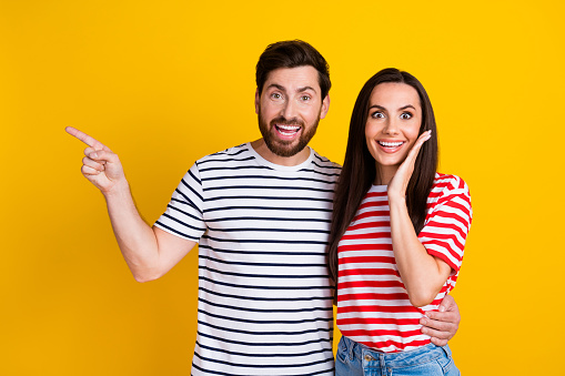 Photo portrait of attractive young couple point excited amazed empty space wear trendy striped clothes isolated on yellow color background.