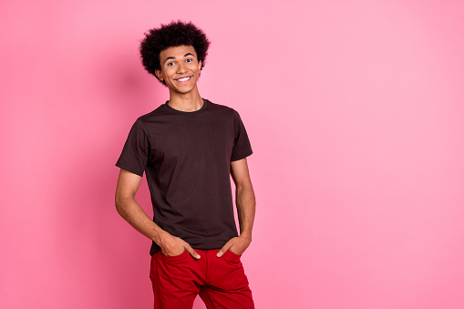 Photo of young attractive guy model in brown t shirt and red pants positively posing casual clothing isolated on pink color background.
