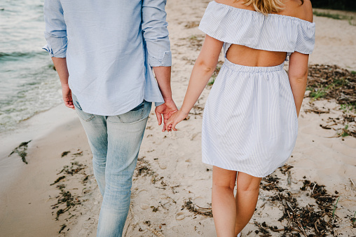 Man and woman walking on sand. Back view. Couple in love holding hands on seashore. Female and male walk on beach ocean and enjoying a sunny summer day on vacation. Bottom down view on legs. Closeup