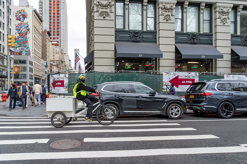 Fifth Avenue, Manhattan, New York, USA - March, 2024. Fifth Avenue street view near Madison Square Park and the Flat Iron building.  In the foreground  is a cycle delivery person and parked cars.