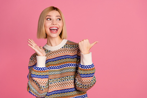 Photo of impressed girl with bob hairstyle wear ornament sweater staring indicating at offer empty space isolated on pink color background.