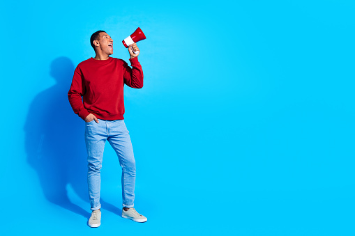 Full length portrait of nice positive person communicate loudspeaker toa empty space isolated on blue color background.