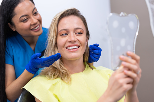 Woman looking at her teeth in the hand held mirror, after dental procedure at dentist's office