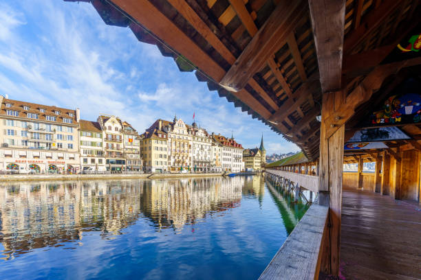 Lucerne, Switzerland - February 22, 2023: View from the Chapel Bridge, the Reuss River and various buildings, in Lucerne (Luzern), Switzerland (paintings are of carnival)