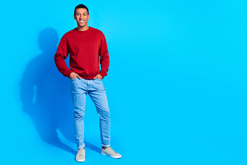 Full length photo of satisfied glad young person put hands pockets posing empty space ad isolated on blue color background.