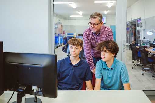 Gen Z teenage high school students coding durning computer lessons, talking with male teacher.